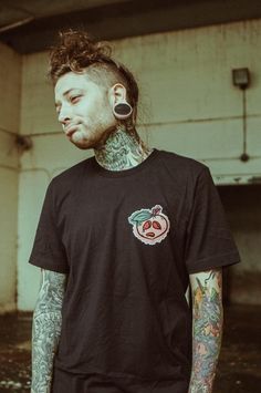 a man with tattoos and piercings standing in front of an old building wearing a black t - shirt