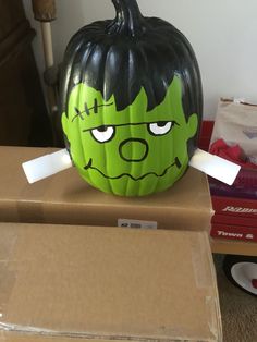 a green and black pumpkin sitting on top of a cardboard box with tape sticking out of it's mouth