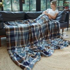 a woman sitting on a couch under a plaid blanket