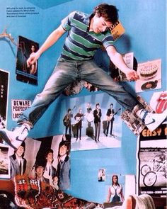 a man jumping in the air on top of a bed with pictures and posters all around him