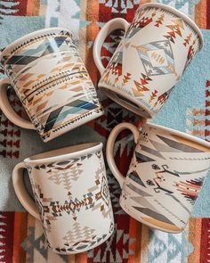 four coffee mugs sitting on top of a colorful table cloth with designs in the middle