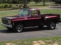 a red pickup truck parked on the side of a road next to a tree and grass covered field