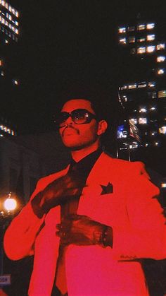 a man in a red suit and sunglasses is standing with his hands on his chest