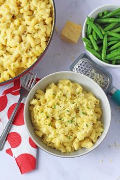 two bowls filled with macaroni and green beans on top of a white table