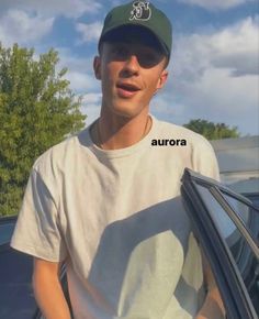 a young man wearing a green hat standing next to a car