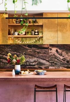 a kitchen with two stools next to a counter and some plants on the wall