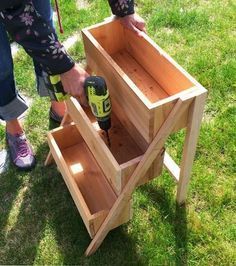 a person is holding a drill and drilling holes in a wooden box on the grass