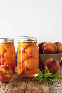 two jars filled with peaches sitting on top of a wooden table next to some fruit