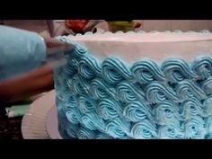 someone is decorating a blue and white cake with icing spirals on it