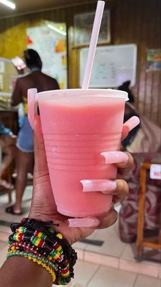 a person holding a pink drink with a straw in it's hand and wearing bracelets