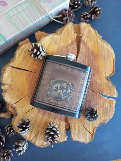 a flask is sitting on top of a piece of wood with pine cones around it