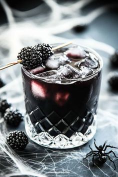 a glass filled with ice and blackberries on top of a table next to some spider legs