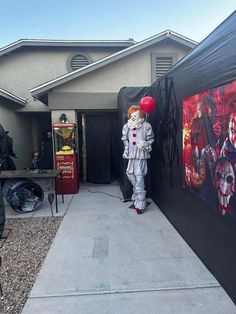 a man in clown costume standing next to a house with balloons on it's head