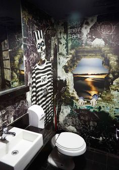 a toilet and sink in a room with graffiti on the walls, along with a wallpapered mural