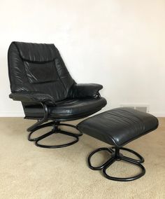 a black leather chair and ottoman sitting on carpeted floor in front of a white wall