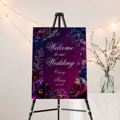 a welcome sign is on an easel next to a vase with flowers and lights