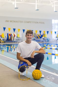 a young man sitting on top of a swimming pool next to a yellow and blue ball