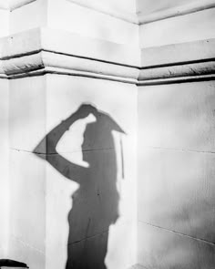 a shadow of a person holding a umbrella on the side of a building with a wall in the background