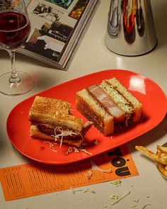 a plate with two sandwiches on it next to french fries and a glass of wine