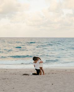 two people are hugging on the beach by the ocean while one person is holding his head