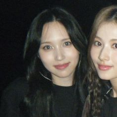 two young women standing next to each other in front of a black background, one with long dark hair and the other with light brown eyes