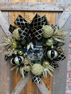 a new year's wreath hanging on the side of a wooden door decorated with gold, black and silver ornaments