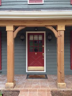 a red front door on a gray house with wooden pillars and arches over the entrance