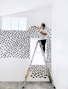 a woman standing on a ladder in front of a wall with black and white tiles