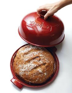 a person is holding a red pot over a loaf of bread