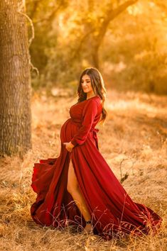 a pregnant woman in a red dress poses for the camera while standing next to a tree