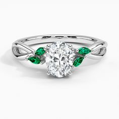 a white gold ring with an oval cut diamond and green leaves on the band, set in