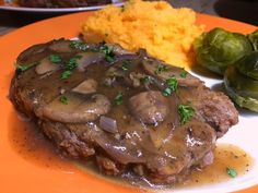 a plate topped with meat covered in gravy next to mashed potatoes and brussel sprouts