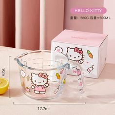 a glass measuring cup with hello kitty on it next to a box and lemon slice