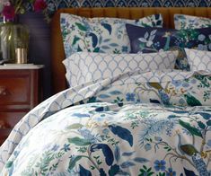 a bed with blue and green floral comforter set on top of it, next to a night stand