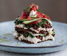 a stack of food sitting on top of a blue plate covered in vegetables and other toppings