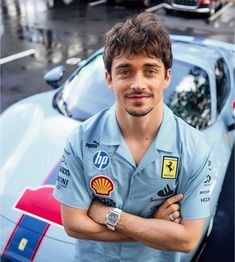 a man with his arms crossed standing in front of a blue sports car on the street