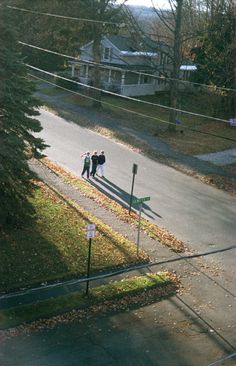 two people are walking down the street in front of some trees and power lines with houses behind them