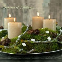 three candles are lit on a tray with moss and pine cones