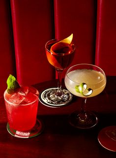 two cocktails sitting on top of a wooden table next to each other in front of a red wall