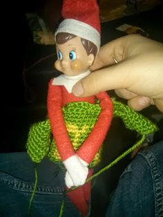 a person holding a knitted elf doll in their lap and wearing a red hat