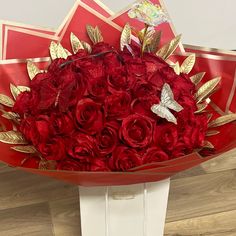 a bouquet of red roses with gold leaves in a white box on a wooden floor