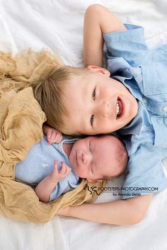 two young children laying next to each other on top of a white sheet covered bed