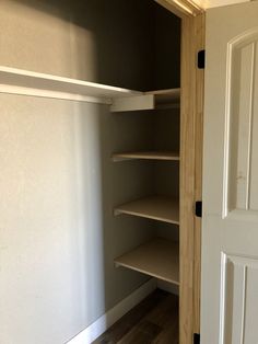 an empty walk in closet next to a white door and wooden floor with shelves on both sides