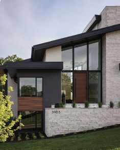 a modern house with white brick and black trim on the windows, grass and trees in front