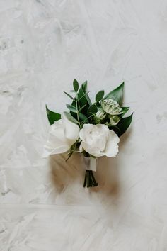 a bouquet of white flowers sitting on top of a white table cloth with green leaves