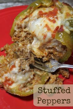 a red plate topped with meat and cheese covered stuffed bell peppers next to a fork