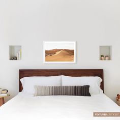 a bed with white sheets and pillows in a bedroom next to two pictures on the wall