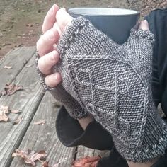 a person holding a cup in their hands on a wooden bench with leaves around them