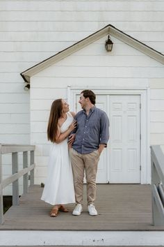 a man and woman standing on a porch next to a white building with a door