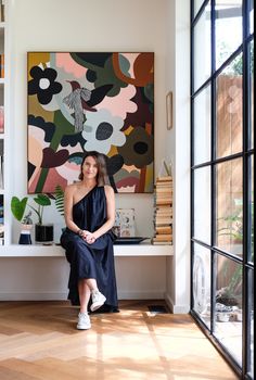 a woman is sitting on the floor in front of a painting and bookshelf